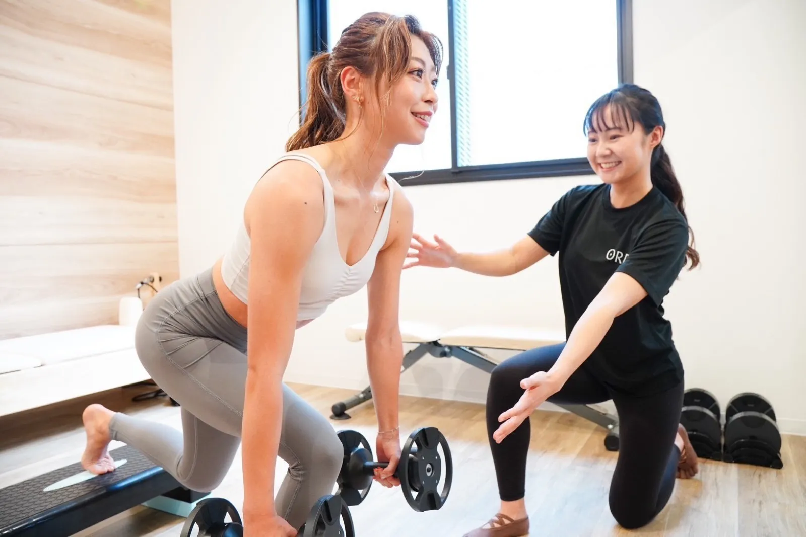 トレーナーのサポートを受けながらダンベルを使う女性